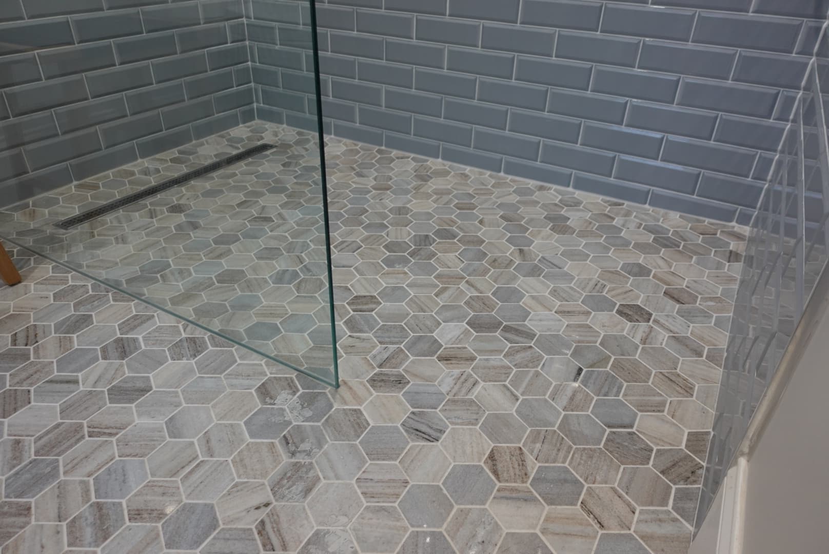 Shower floor with hexagon tiles of varying shades of blue and tan. Shower walls are a light blue subway tile with white grout